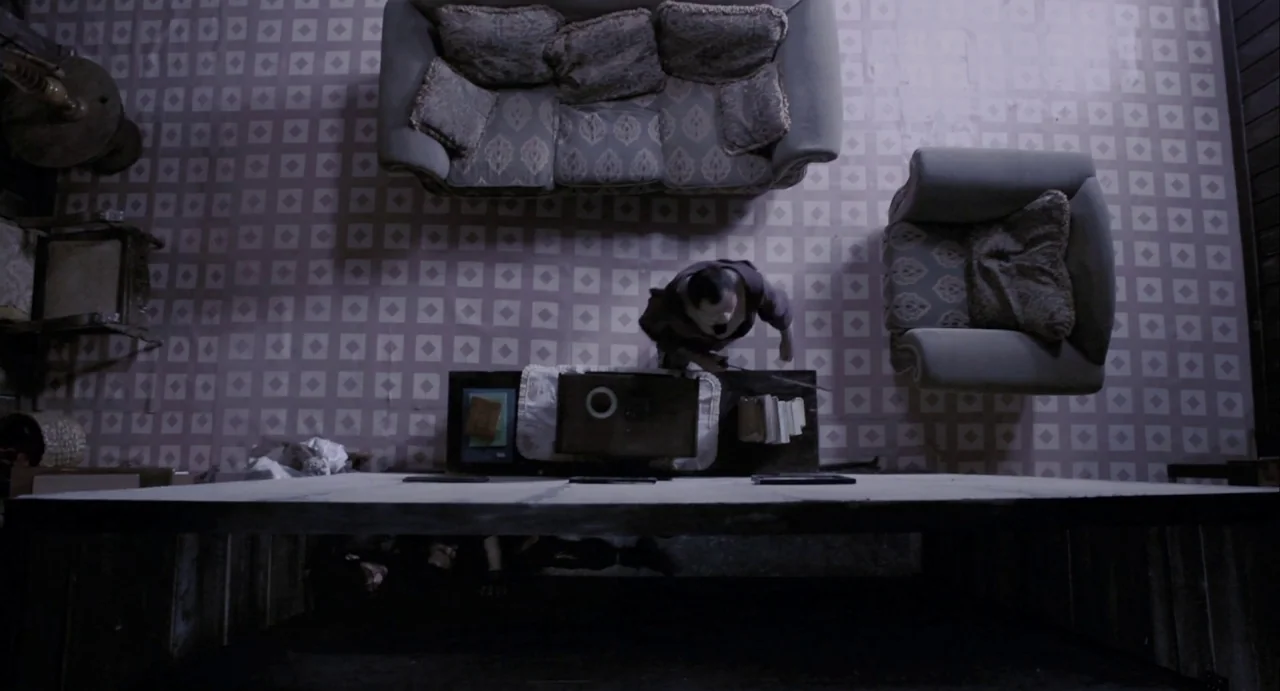 The Raid (2012) movie still: wide — A top-down view shows a room with patterned tile floors and arranged furniture. A person stands near a table…