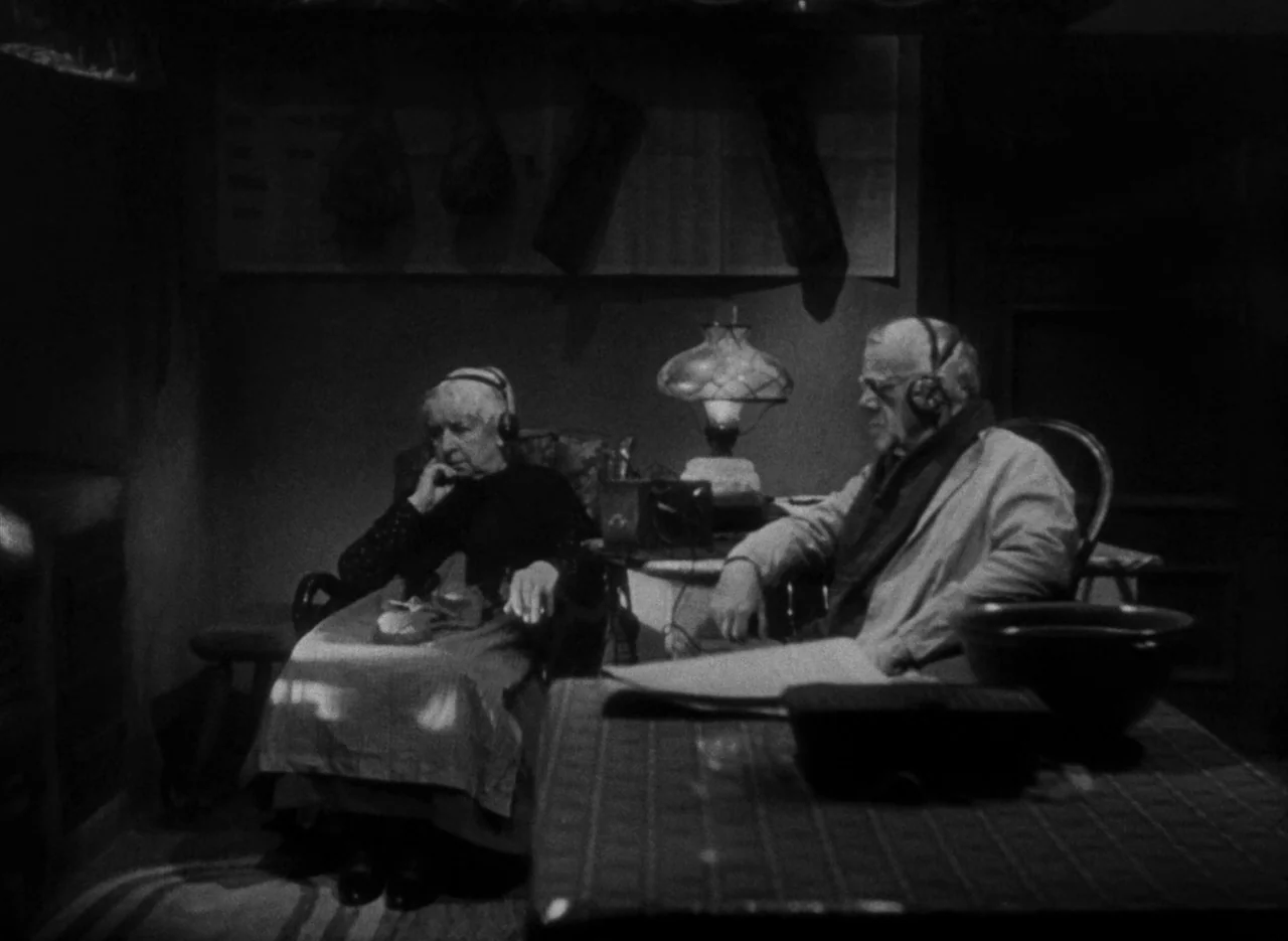 The Invisible Man (1933) (1933) movie still: medium — A dimly lit room contains two elderly people sitting in chairs with audio headphones on. They…