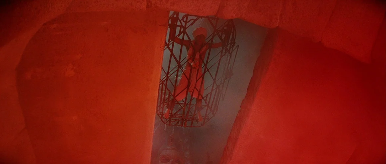 Indiana Jones and the Temple of Doom (1984) movie still: wide — A stone temple chamber is bathed in intense red light from an unseen source. A man…
