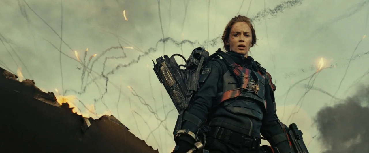 Edge of Tomorrow (2014) movie still: medium — A war-torn exterior landscape filled with smoke trails and fire debris under a cloudy sky. A woman in…