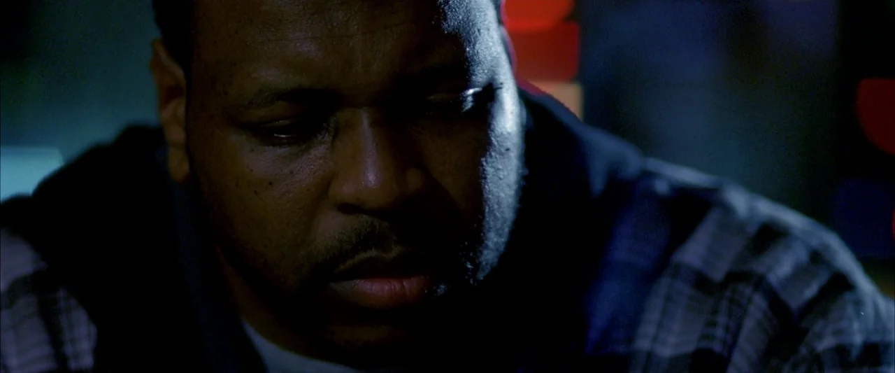 Ballast (2008) movie still: closeup — A man stands outdoors at night near glowing red city street lights. He looks down with a neutral expression…