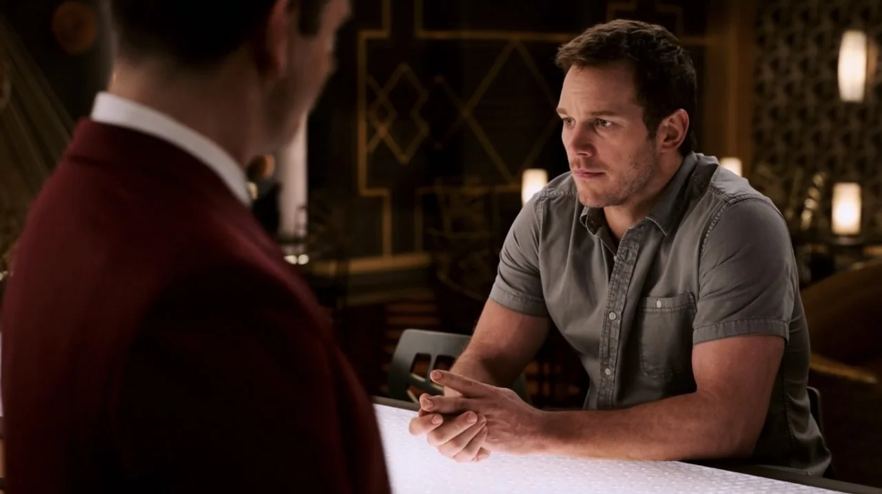 Passengers (2016) movie still: medium — A dimly lit lounge with patterned walls and a brightly illuminated bar top. A man in a grey shirt sits at…