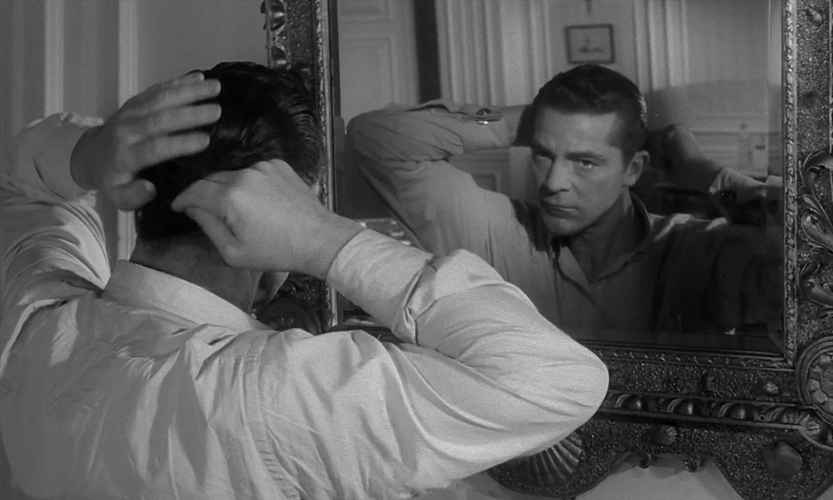 Night Of The Demon (1957) movie still: medium — A man stands before a large, highly decorative baroque-style mirror in a bright room. He examines…