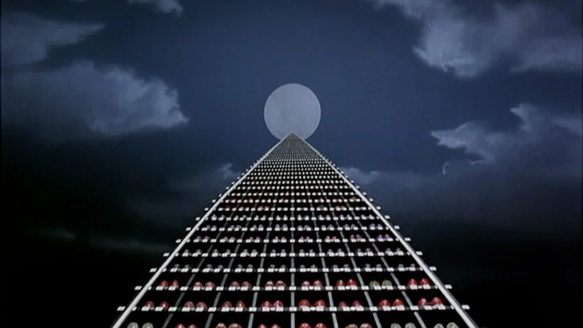 The Big Lebowski (1998) movie still: establishing — A vast grid of red spheres recedes into the distance beneath a dark, cloudy sky. A large,…