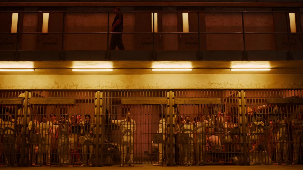 The Laundromat (2019) movie still: wide — A multilevel correctional facility features iron barred cells containing numerous inmates in white…