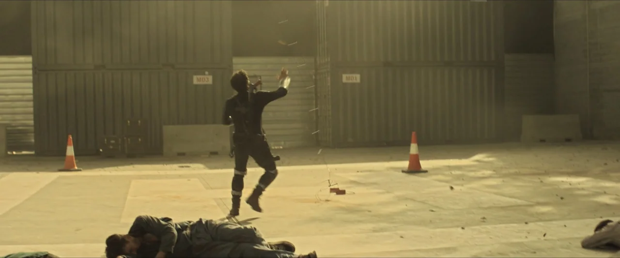 Apocalypse Z: The Beginning of the End (2024) movie still: wide — A dusty outdoor loading dock with shipping containers and orange traffic cones.