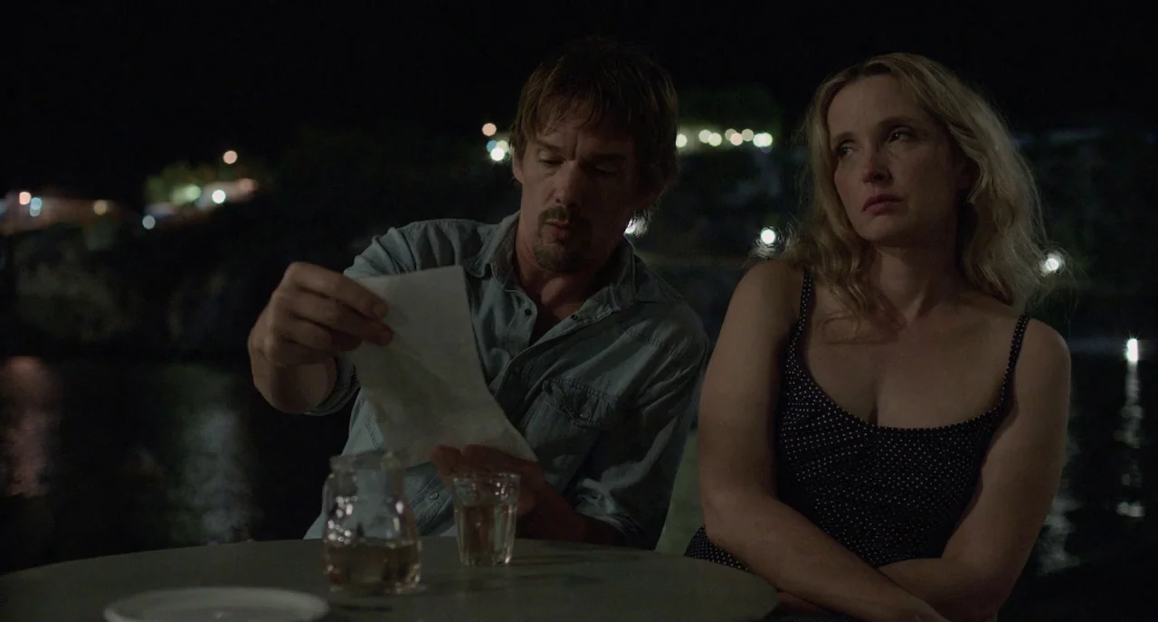 Before Midnight (2013) movie still: medium — A nighttime outdoor cafe overlooking a dark body of water with distant lights. A man in a denim shirt…