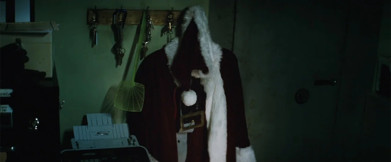 Run All Night (2015) movie still: medium — A dimly lit office features a Santa suit hanging on a wall-mounted hook. A fly swatter and various keys…