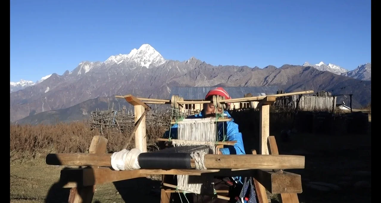 Blutch (2018) movie still: medium — A person weaves on a wooden loom in a mountainous rural field under clear skies. The subject works at the loom…