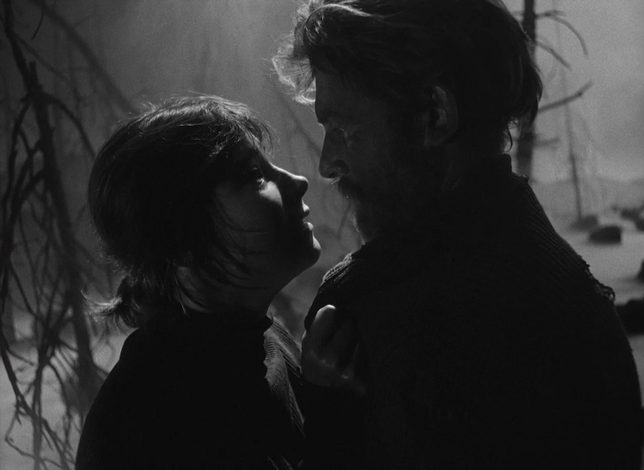 Letter Never Sent (1960) movie still: medium — A dark, barren landscape with skeletal trees at night serves as the backdrop. A man and a woman stand…