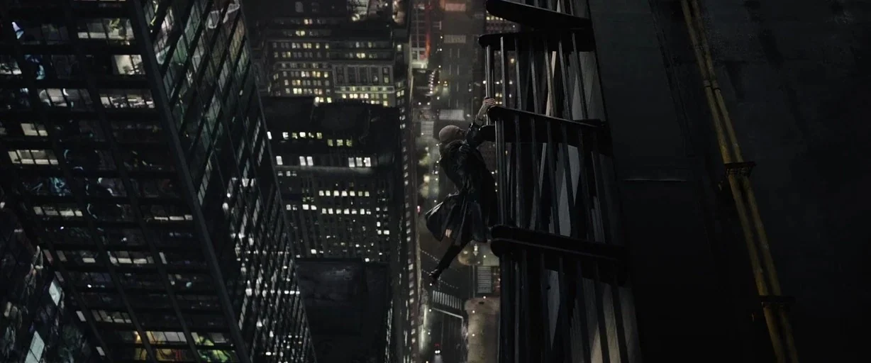 Shazam! (2019) movie still: wide — A high-angle view looks down a dark metal fire escape attached to a skyscraper. A man in a dark trench coat…