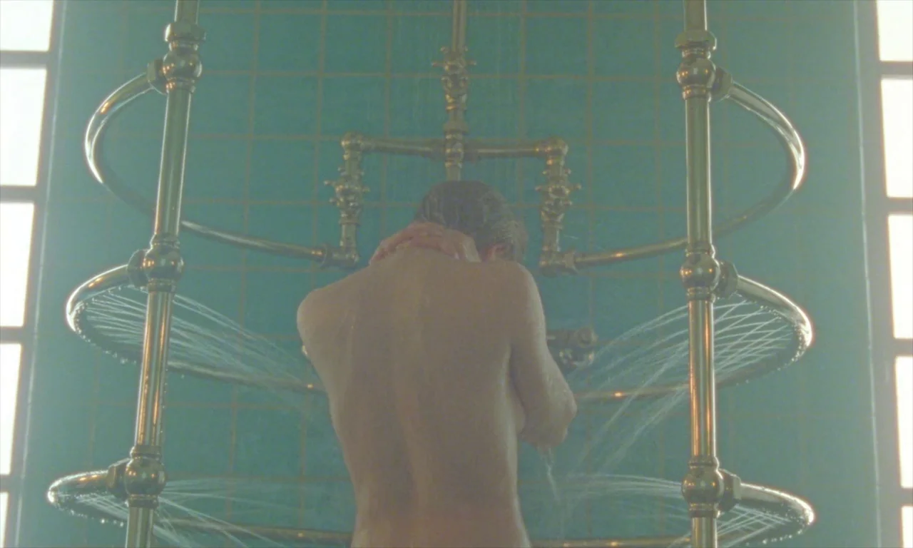 Spencer (2021) movie still: medium — A teal-tiled stall features an elaborate, circular gold-colored shower fixture with multiple water sprays. A…
