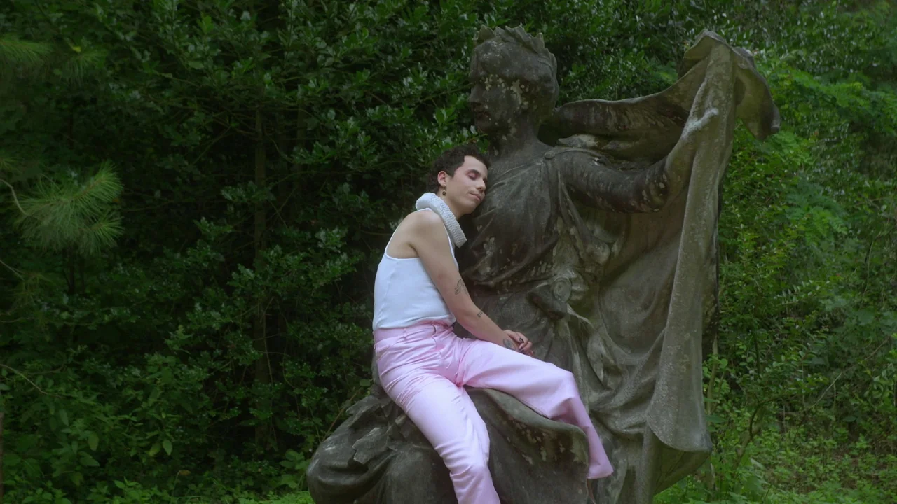 Orlando: My Political Biography (2023) movie still: medium — A dense patch of green forest contains a large, weathered, carved stone female figure.…
