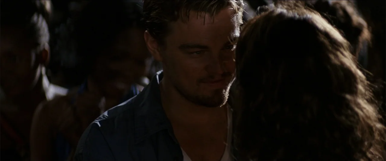 Blood Diamond (2006) movie still: closeup — A dark, crowded social space with blurred background figures visible in the periphery. A man with light…