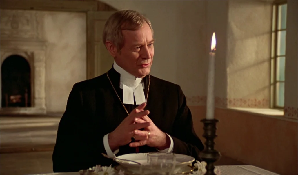 Fanny and Alexander (1982) movie still: medium — A man in clerical clothing sits at a table in a bright, sparsely furnished room. A lit candle…
