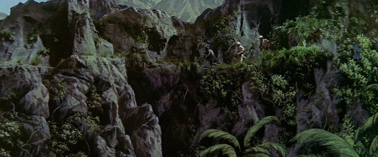 King Kong Vs. Godzilla (1962) movie still: wide — A narrow mountain trail winds through steep, jagged rocky cliffs covered with dense vegetation.…