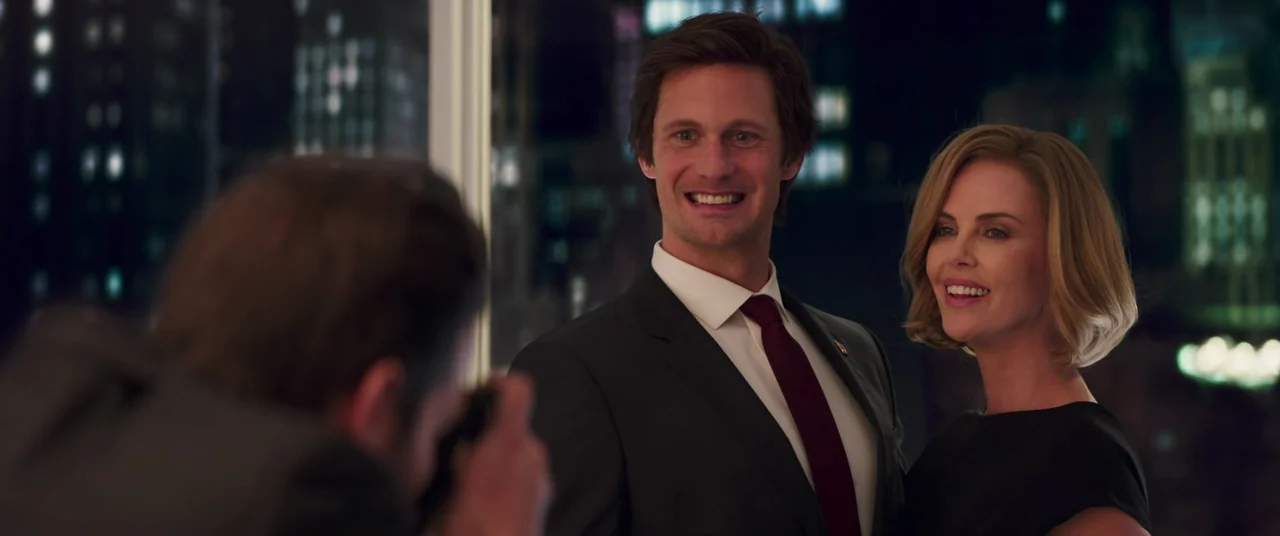 Long Shot (2019) movie still: medium — A dark, modern interior features large windows overlooking a blurred city skyline at night. A man in a suit…