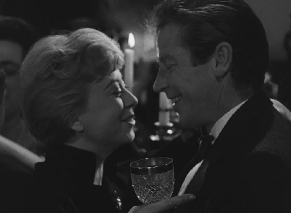 Il Bidone (1955) movie still: medium — A dark indoor space with a lit candle glowing in the blurred background. A woman and a man look toward each…