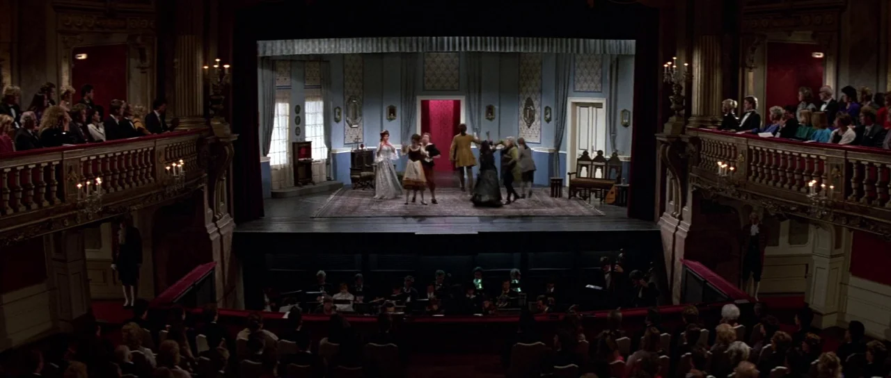 The Living Daylights (1987) movie still: wide — An opulent 19th-century theater features a stage set designed as an indoor parlor. Actors in period…