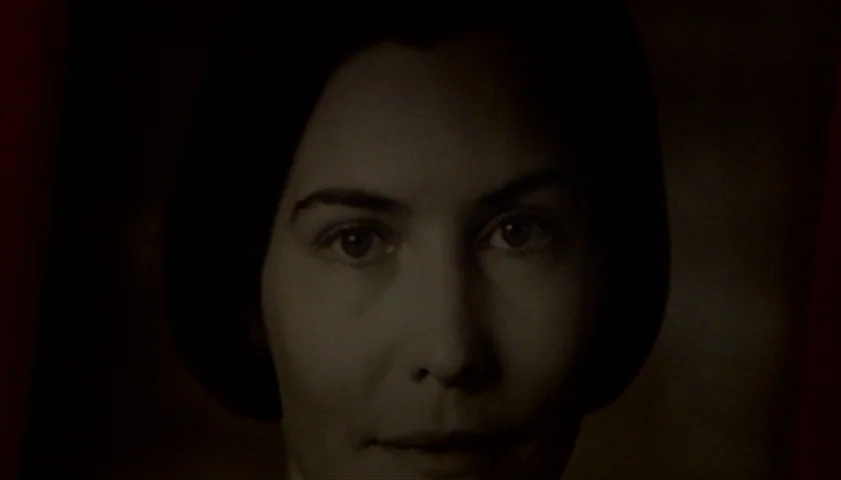 Saraband (2003) movie still: closeup — A dark, plain background frames a woman's head and shoulders. The woman looks directly forward with a steady…