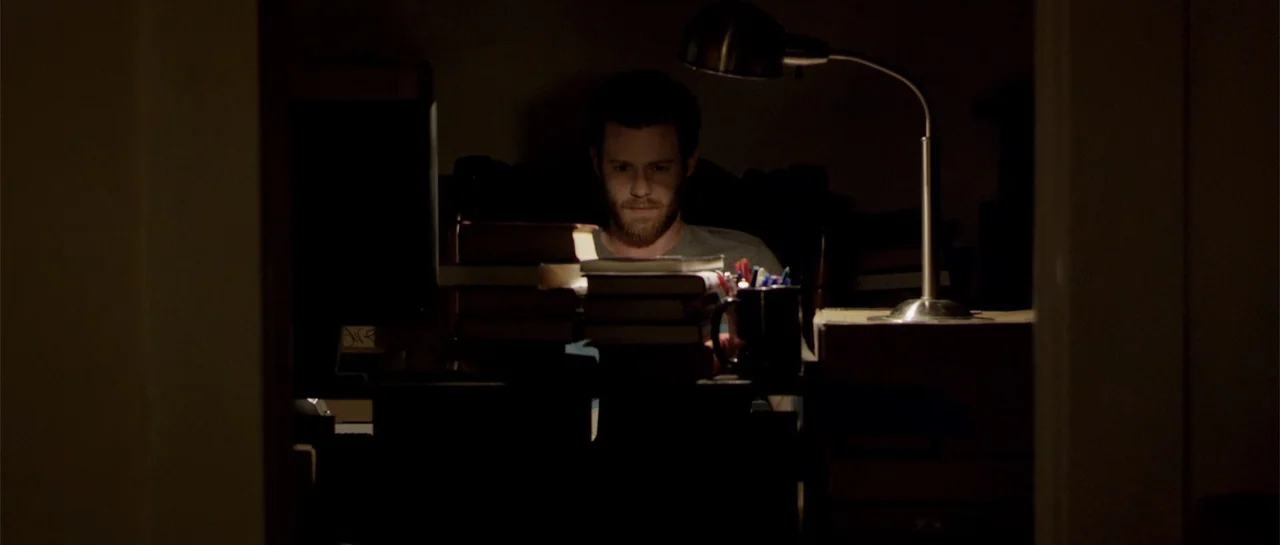 Night People (1954) movie still: medium — A dark study contains a desk cluttered with stacked books and a metallic lamp. A man sits at the desk…