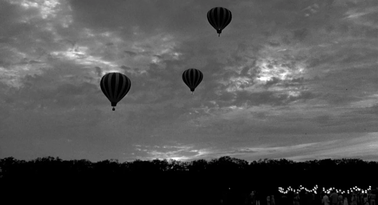Stardust Memories (1980) movie still: wide — Three hot air balloons drift across a clouded sky at twilight above a field. A group of people stands…