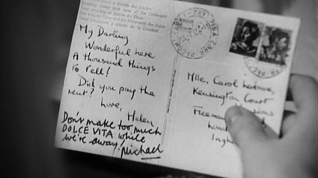 Repulsion (1965) movie still: closeup — A close-up shot of a vintage postcard being held by a human hand. The card contains handwritten text…