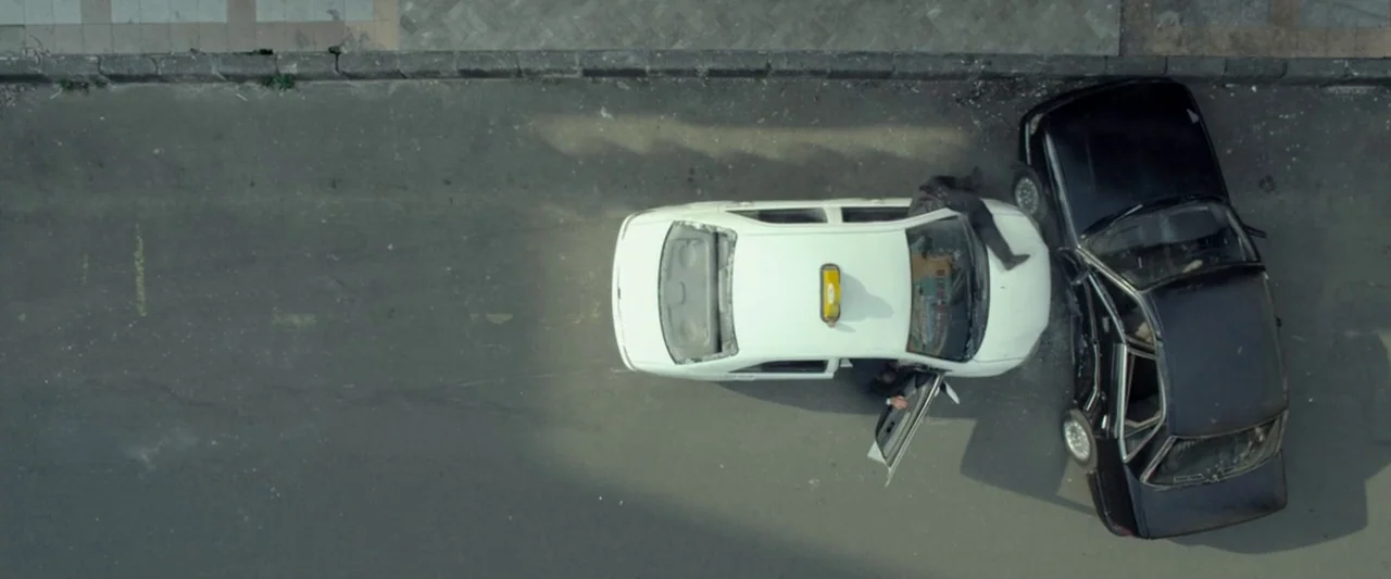 The Raid 2 (2014) movie still: wide — An asphalt road serves as the location for a violent vehicle collision. A black sedan is crashed into the…