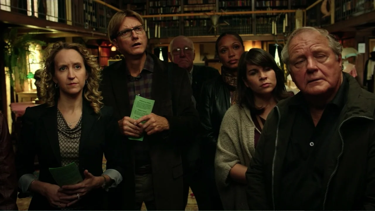Ghostbusters (2016) movie still: medium — A group of people stand inside a dark wood-paneled library filled with bookshelves. The individuals gaze…