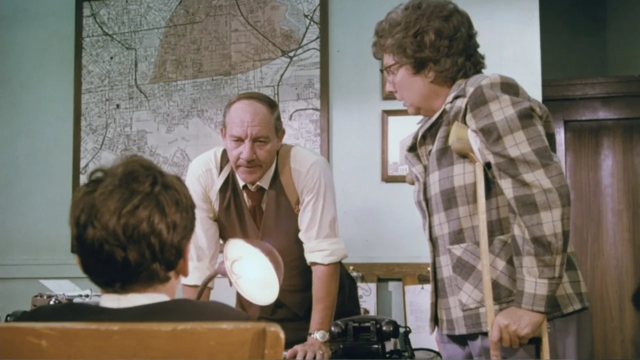 Aunt Mary (1979) movie still: medium — A cluttered office features a large wall-mounted map and vintage furniture. An older man in a vest consults…