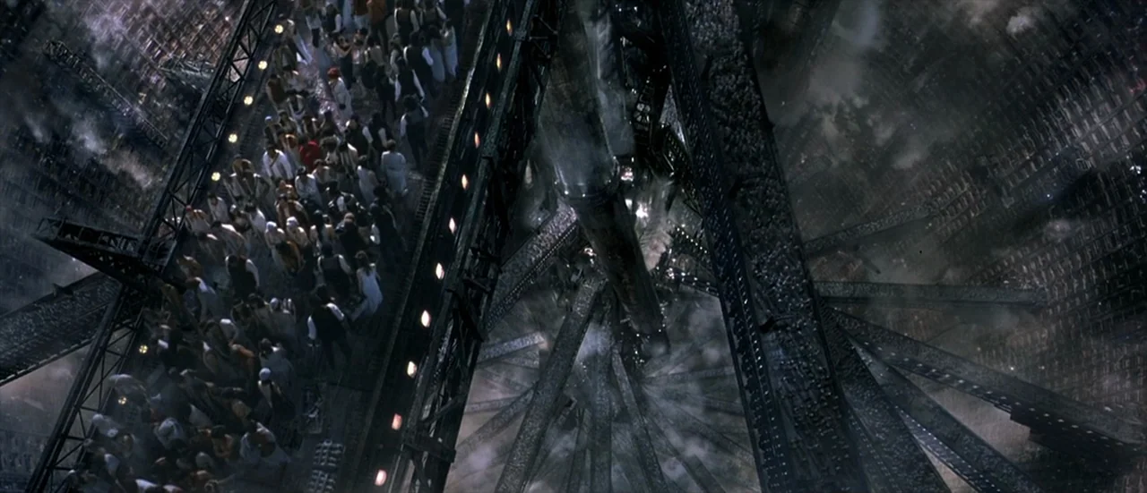 The Matrix Revolutions (2003) movie still: wide — A dense crowd of people navigates narrow steel walkways suspended over an industrial abyss. Steam…