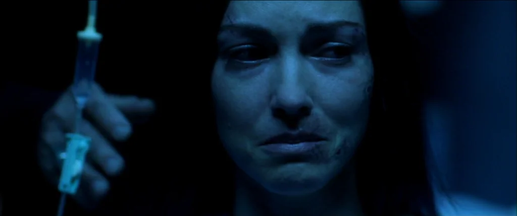 Kill Bill Vol. 1 (2004) movie still: closeup — A dark hospital room is bathed in low-key blue light. A woman with visible facial bruising stares…