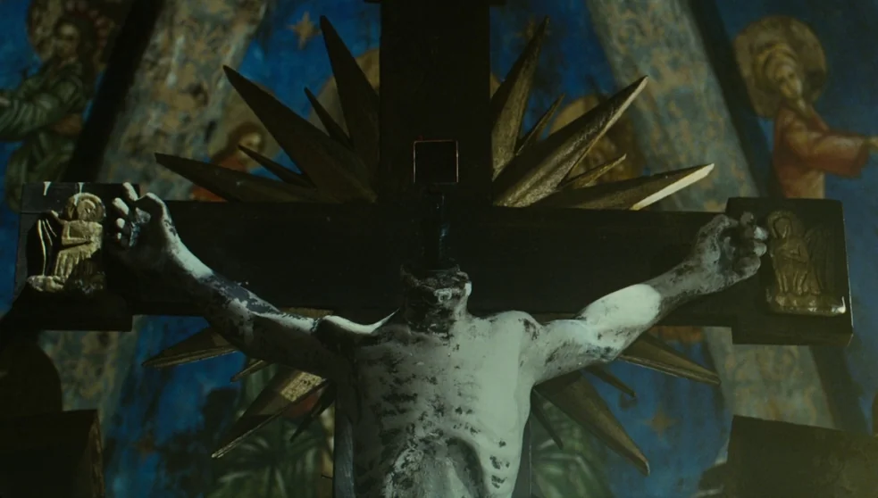 The Zero Theorem (2013) movie still: medium — A dimly lit church interior features a headless religious statue mounted on a cross. The background…