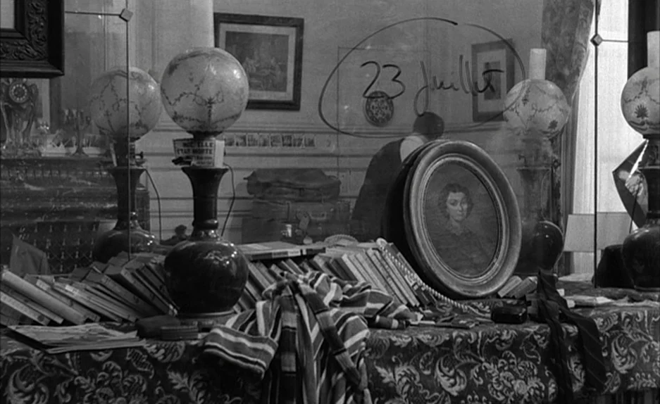 Le Feu Follet (1963) movie still: medium — A cluttered surface features ornate lamps and books in a lived-in room. A date is handwritten onto the…