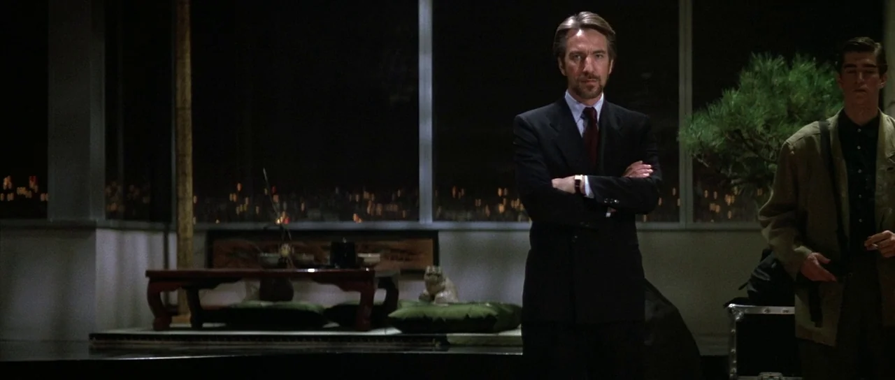 Die Hard (1988) movie still: medium — A dark, modern high-rise interior features large windows overlooking a sprawling city at night. An elegant man…