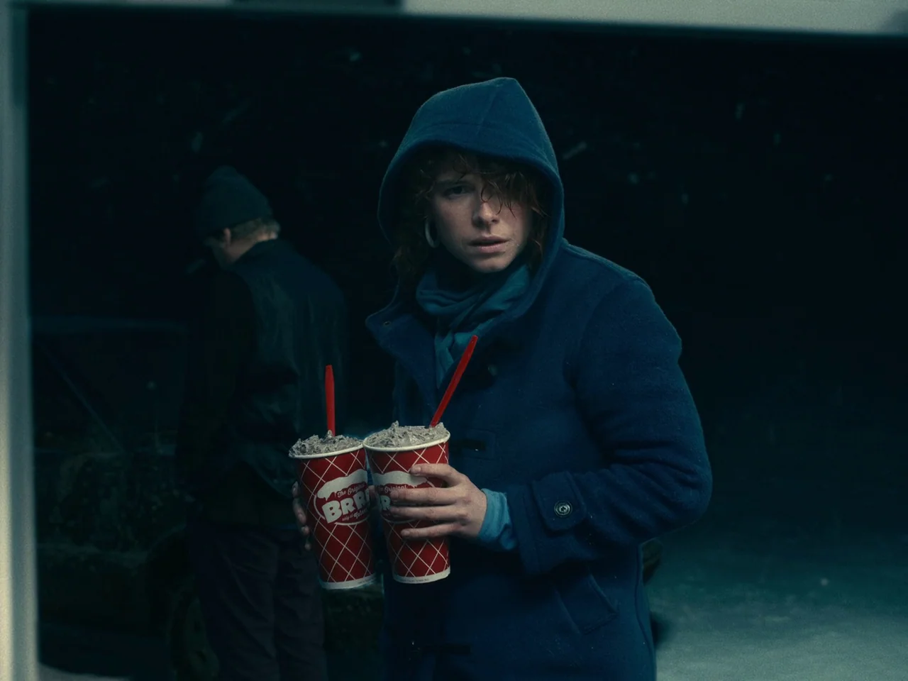 I’m Thinking of Ending Things (2020) movie still: medium — A dark outdoor setting at night with a distant silhouetted figure near a vehicle. A woman…