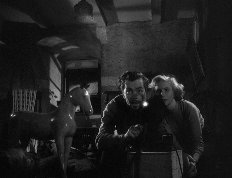 Prison (1949) movie still: medium — A cluttered nursery features floral-patterned walls and a wooden rocking horse in the foreground. A man and…