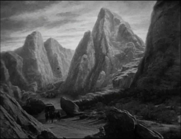 Dracula (1931) movie still: establishing — A rugged desert canyon features towering, jagged rock formations under a cloudy sky. A small stagecoach…