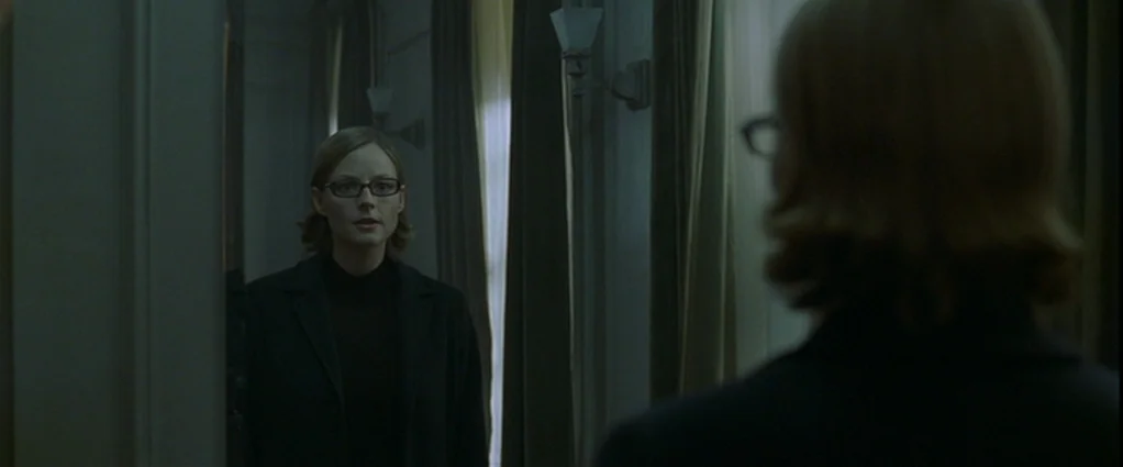 Panic Room (2002) movie still: medium — A dimly lit indoor corridor has dark curtains and mounted wall light fixtures. A woman wearing glasses…