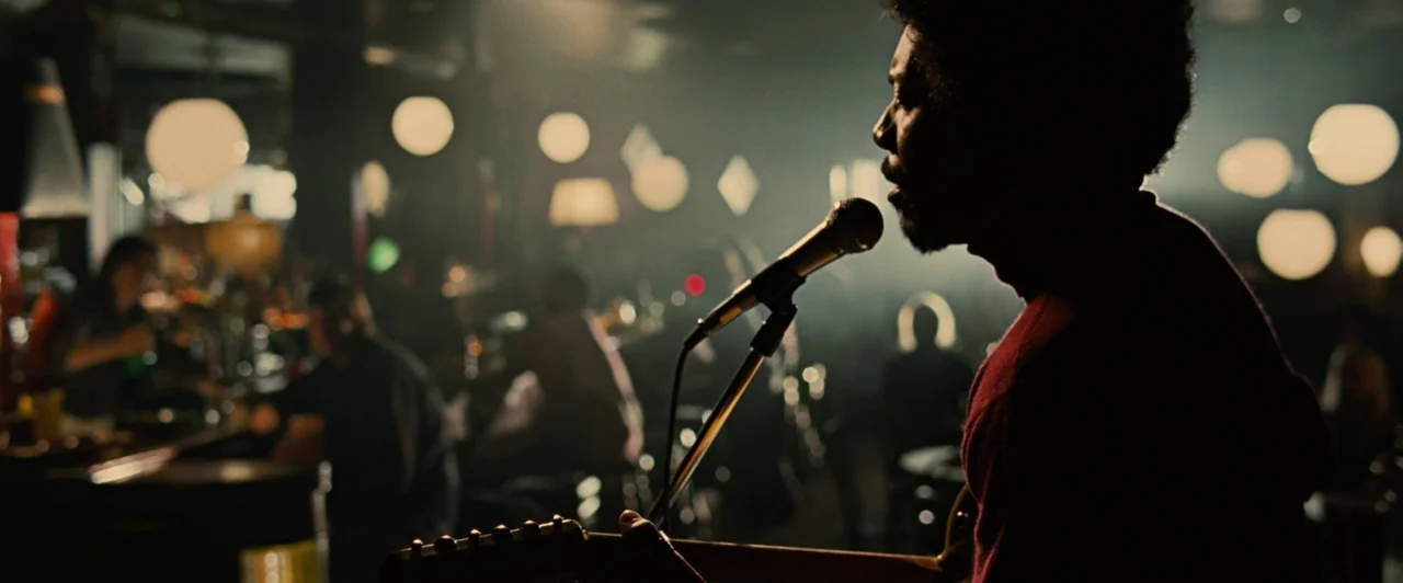 Across the Universe (2007) movie still: medium — A dimly lit bar with numerous spherical lamps in the blurred background. A male singer performs at…