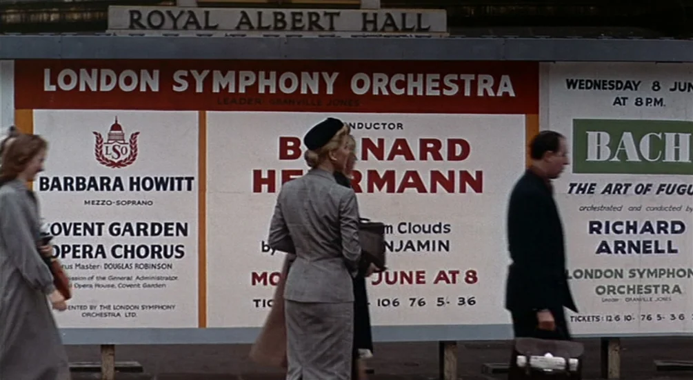 The Man Who Knew Too Much (1956) movie still: wide — A large concert advertisement board stands prominently on a London street in the fifties.…