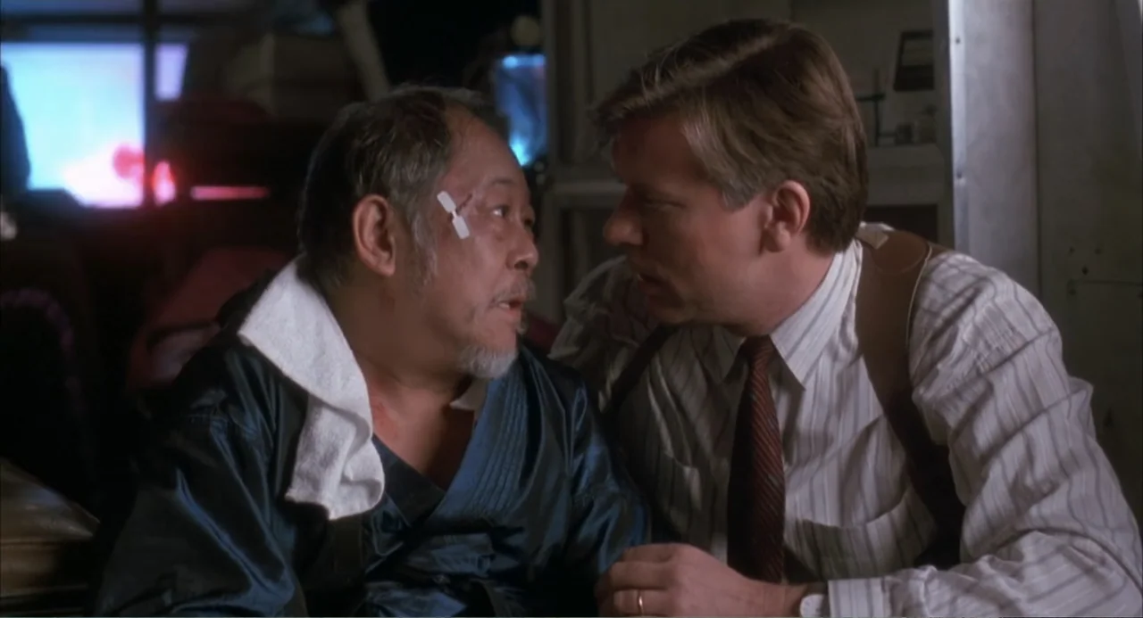 3 Ninjas (1992) movie still: medium — A dimly lit vehicle interior provides a contained space for a quiet conversation. An older man with a facial…