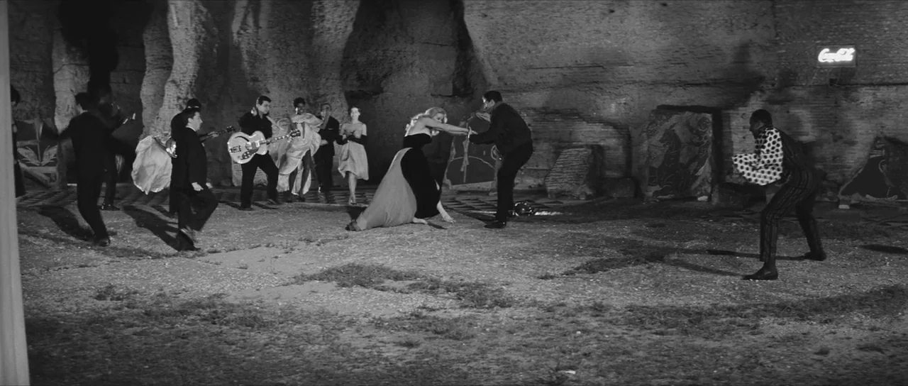 La Dolce Vita (1960) movie still: wide — A spacious stone quarry at night with uneven ground and rough textured walls. A group of formally dressed…