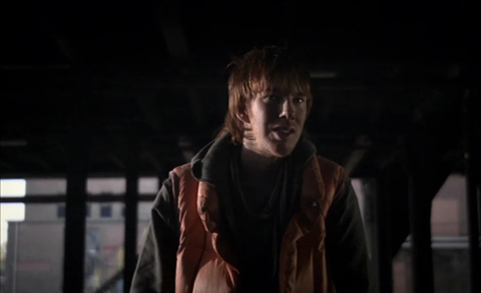 Dear Wendy (2005) movie still: medium — An industrial space with dark steel framing and visible windows in the distance. A man stands in the…