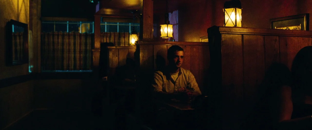 Kiss of the Damned (2012) movie still: medium — A dimly lit restaurant interior features dark wooden booths and amber hanging pendant lights. A…