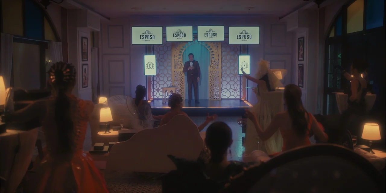Ten Little Mistresses (2023) movie still: wide — A dimly lit room with several small tables and guests facing a central stage. A man in a suit…