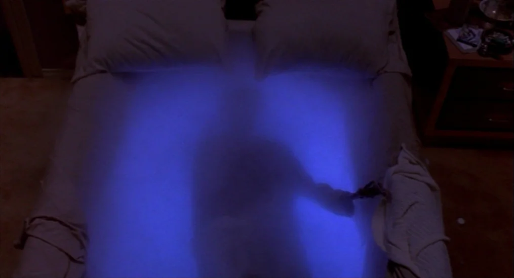 A Nightmare On Elm Street (1984) movie still: medium — A dark, carpeted bedroom contains a bed covered in white linens. An intense blue light…