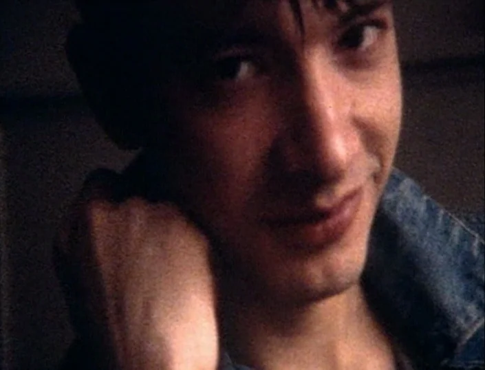 Glitterbug (1994) movie still: closeup — A dimly lit indoor space featuring a close-up of a person's face. The subject rests their chin on their…