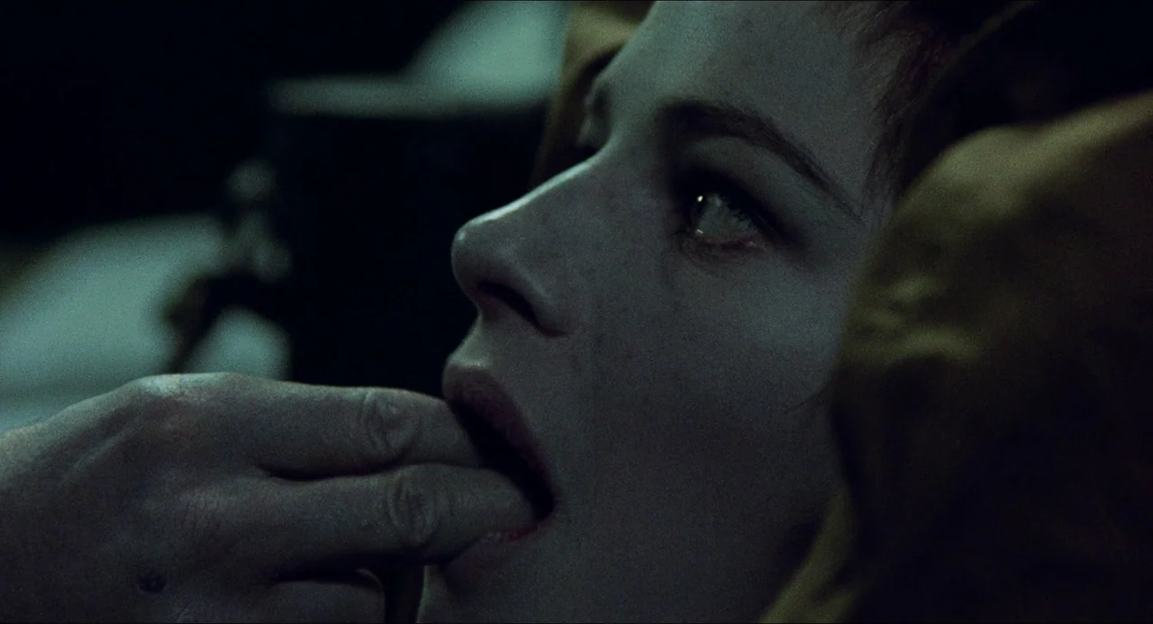 The Night Porter (1974) movie still: closeup — A close-up view of a person in a dim, shadowed indoor environment. The subject has their fingers…