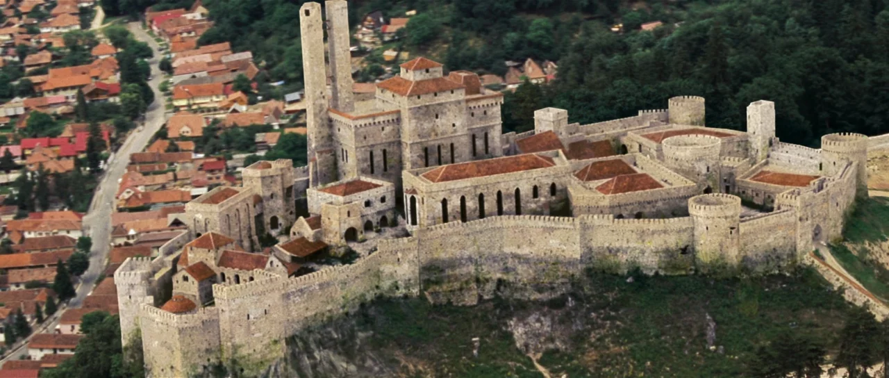 Wanted (2008) movie still: establishing — A massive medieval stone castle sits atop a rugged hill overlooking a small village. The fortress complex…